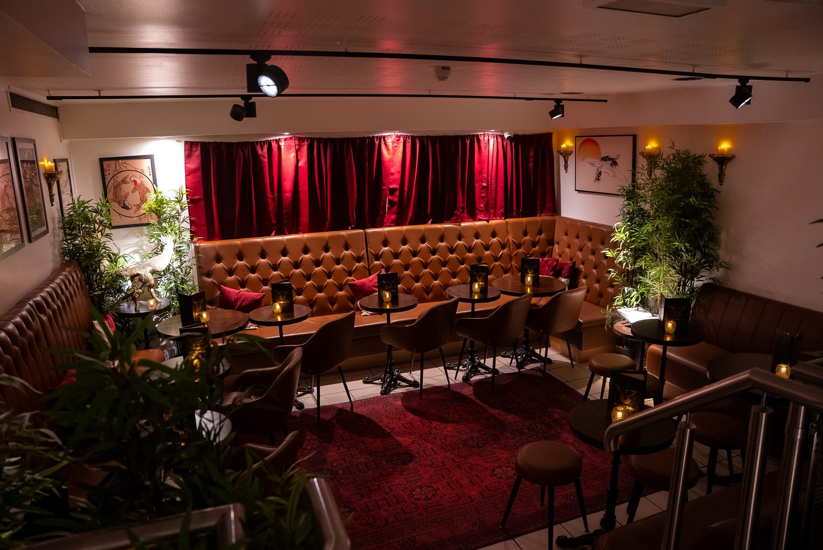 The lounge at Brass Dove — tufted leather banquettes and low tables beneath red curtains