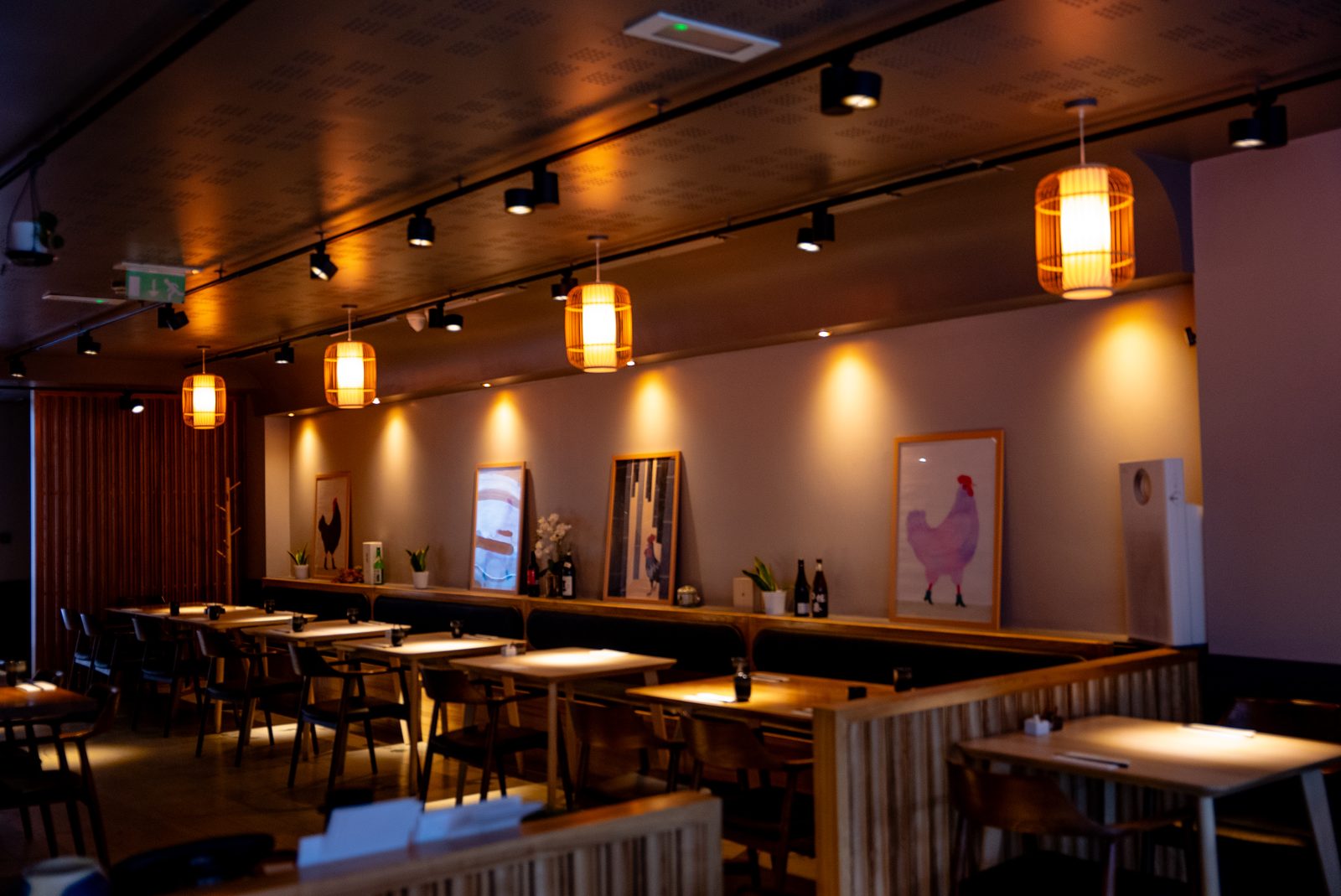 Hotori's ground floor set for a private party — long tables under pendant lamps, the wall of framed prints behind