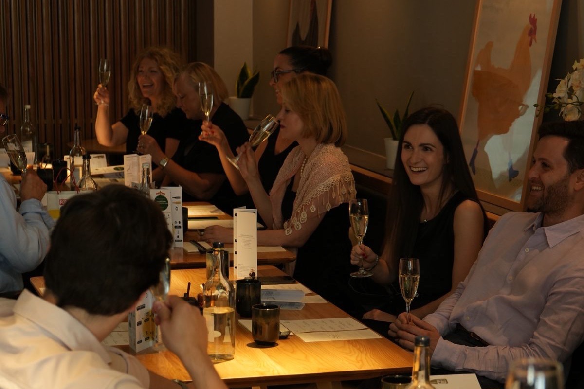 A group of guests laughing over sparkling wine at a long table at Hotori