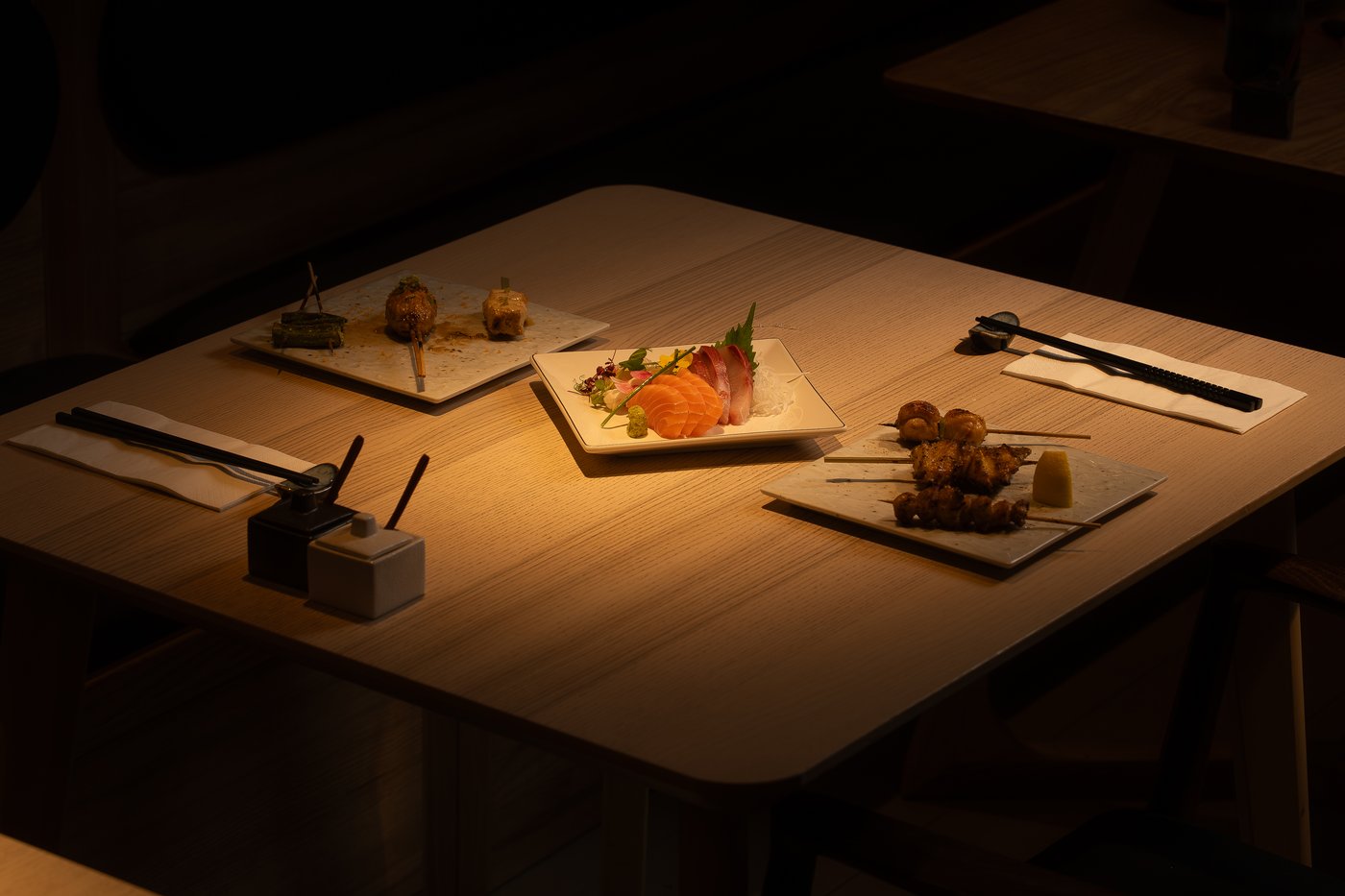 A spotlit table at Hotori with sashimi, salmon, and yakitori skewers in the evening
