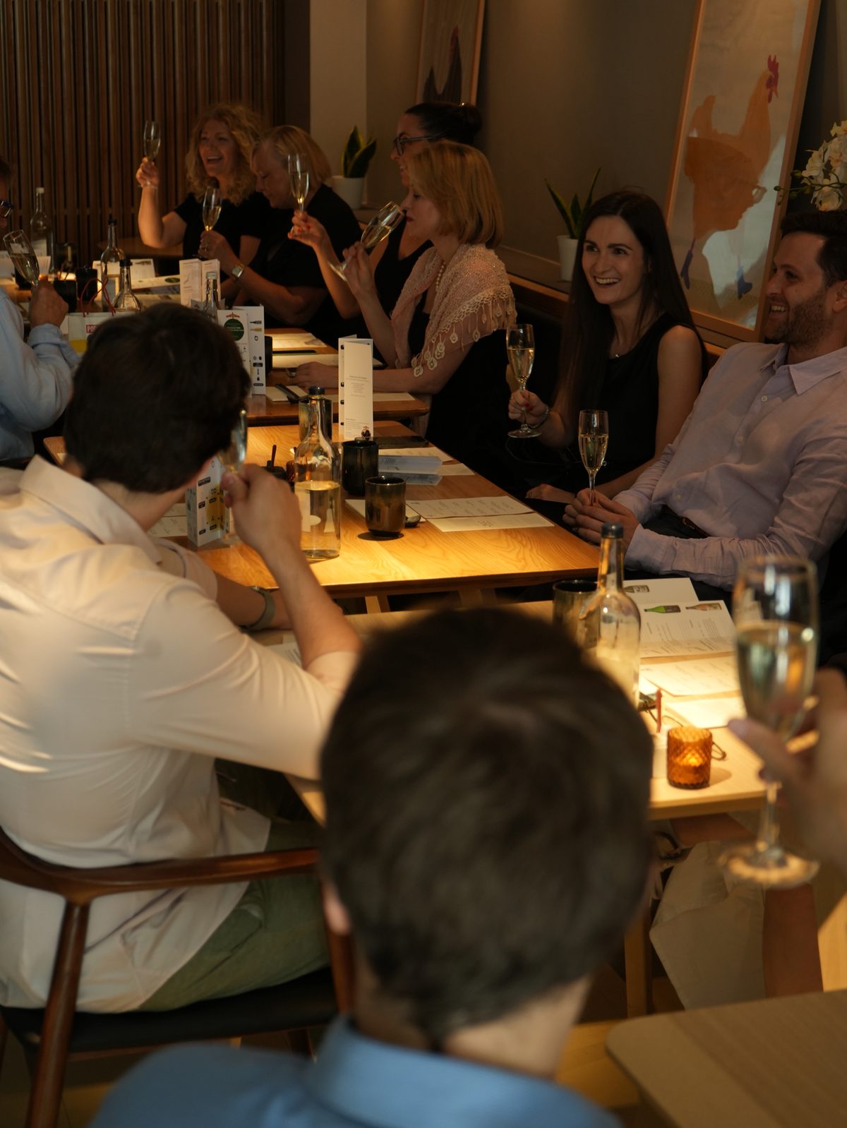 A group of guests laughing over sparkling wine at a long table at Hotori