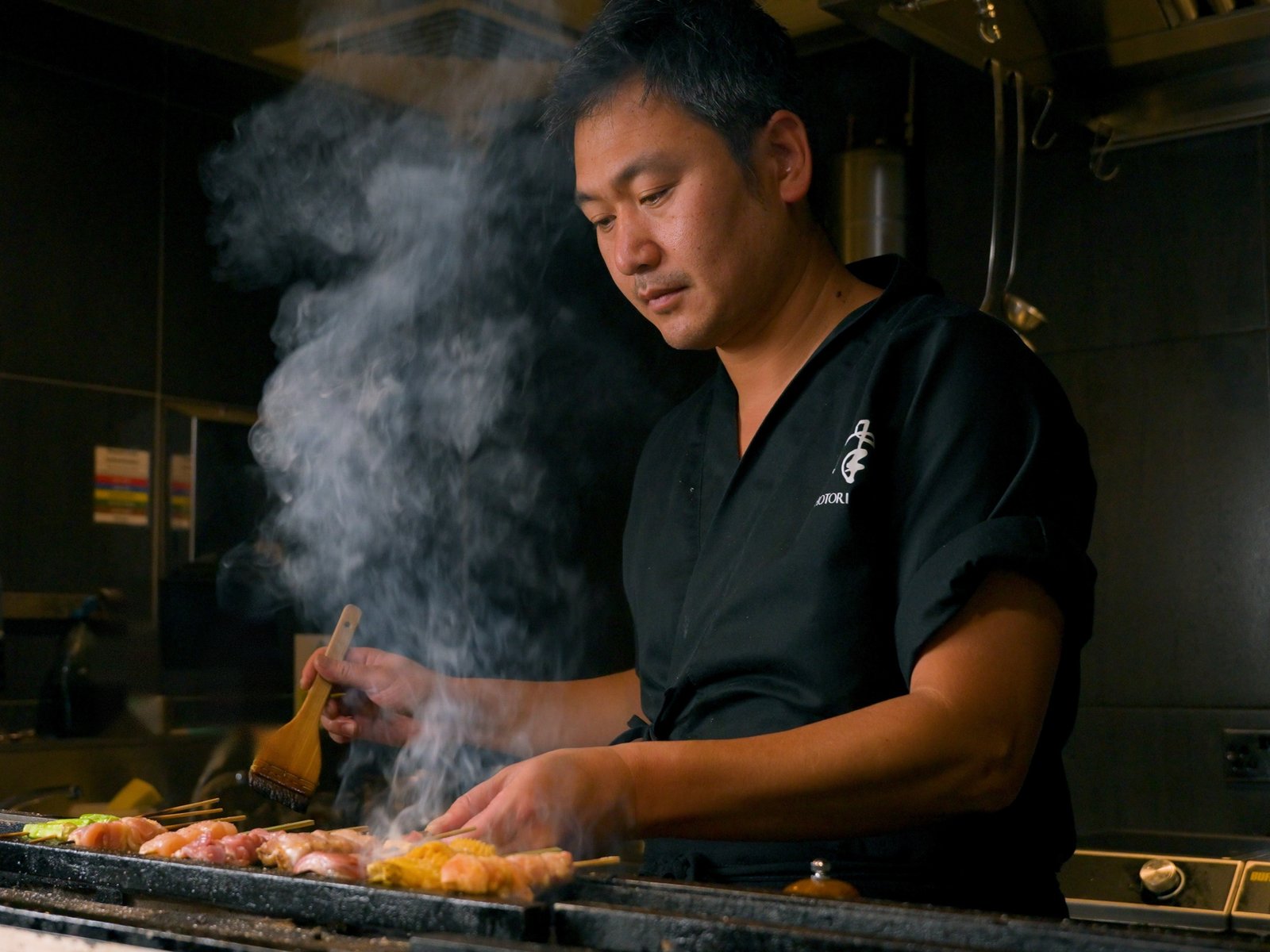 Hotori head chef brushing tare onto yakitori skewers over a binchotan charcoal grill